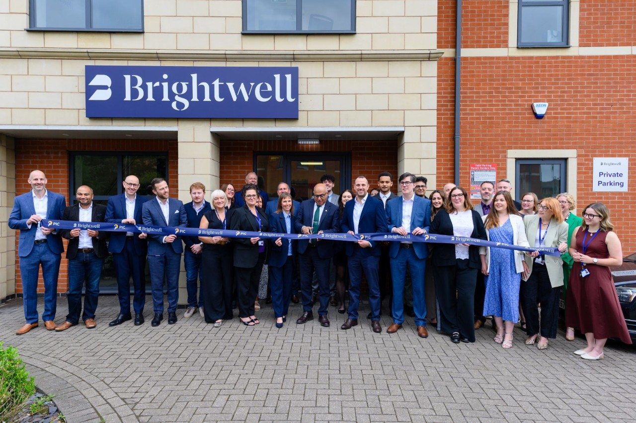 People stood outside office posing for camera about to cut ribbon for opening 