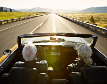 elderly couple driving a convertable soft top sports card heading towards the sunset